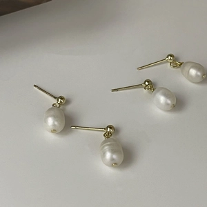 Close-up of golden ball stud earrings with natural baroque freshwater pearl pendants