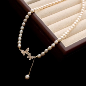 Détail du collier de perles avec pendentif papillon doré orné de diamants étincelants
