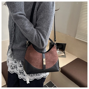 Detail of contrast suede shoulder bag with golden lock on a model in a cozy setting
