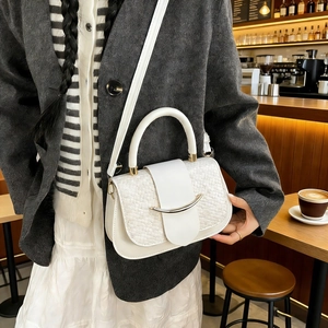 Detail of cream-colored shoulder bag featuring woven texture and gold curved metal buckle