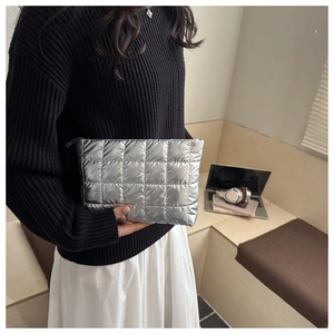 Close-up of a silver quilted puffer clutch bag with metallic finish and black zipper