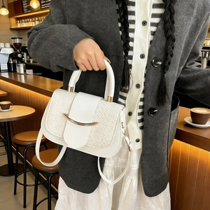 Detail of woven texture beige handbag with gold hardware held by a model in a cafe