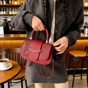 Detail of burgundy woven texture handbag with golden metallic hardware in a cafe