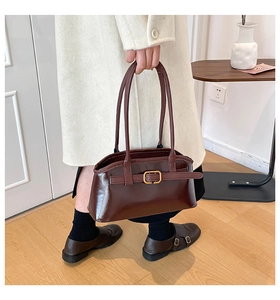 Detail der dunkelbraunen Lederhandtasche mit goldener Schnalle auf minimalistischem Hintergrund