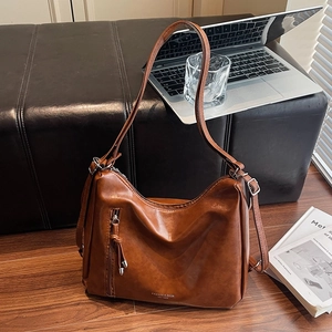 Retro brown leather hobo tote bag with zipper tassel on a warm wood floor background