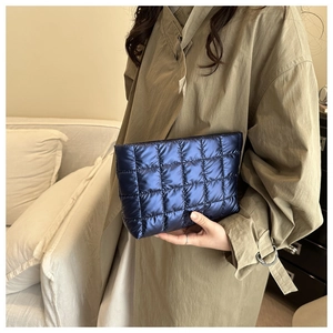 Detail of metallic blue quilted clutch bag held by model wearing a khaki trench coat
