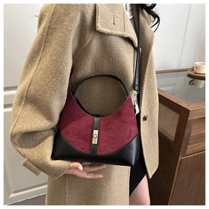 Detail of burgundy suede and black leather bag with gold clasp shown on a trench coat