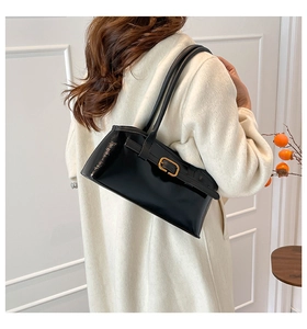 Detail einer schwarzen Lackleder-Schultertasche mit goldener Schnalle an einem Modell
