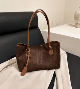 Détail d'un sac cabas en daim marron foncé avec un gland décoratif et de fines bandoulières