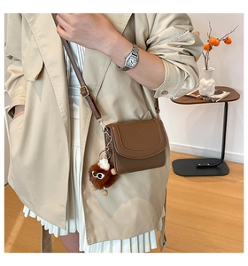 Close-up of brown litchi grain small crossbody bag with a cute plush monster pendant