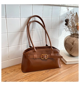 Detail der braunen Leder-Schultertasche mit goldener Schnalle auf Holztisch