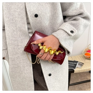 Detail of burgundy patent leather evening bag with unique gold wavy metal handle