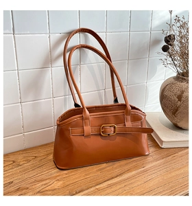 Karamellbraune Leder-Schultertasche mit Schnallendetail auf rustikalem Holztisch