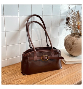 Detailansicht der dunkelbraunen Kunstleder-Schultertasche mit Goldschnalle auf Holztisch