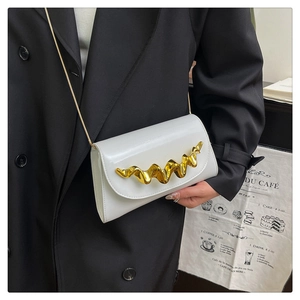 Detail of white patent leather evening bag featuring a bold wavy gold metal ornament