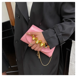 Detail of pink glossy clutch bag with wave-shaped gold metal handle and chain strap