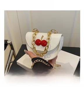 Detail of white semi-circle crossbody bag with red cherry charm and gold chain
