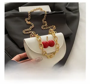 Close-up of textured white crossbody bag with 3D red cherry charms and gold chain strap