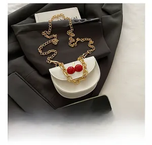 Detailed view of white saddle bag with cherry decor and double gold chain straps