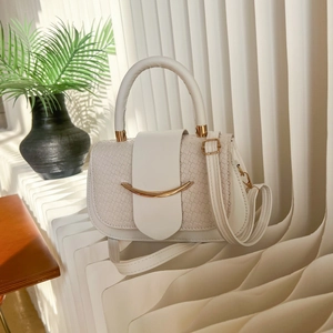 Sac à bandoulière minimaliste blanc cassé avec détails dorés sur banc ondulé