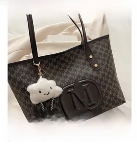Detail of embossed logo and letter print on brown faux leather tote bag with plush charm