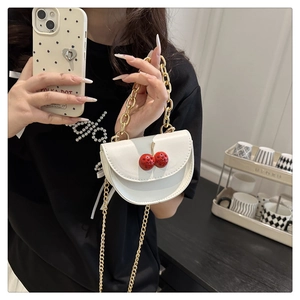 Close-up of white leather handbag featuring 3D red cherry accents and gold chain strap