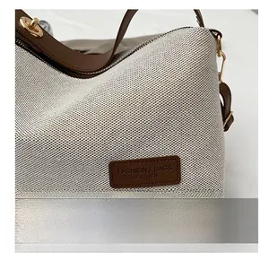 Close-up of beige woven canvas bag with brown leather trim and golden metal clasp detail