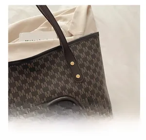 Close-up of brown tote bag with M-letter pattern and white plush bear charm detail