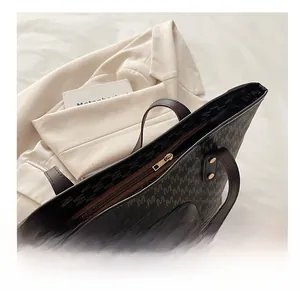 Close-up of smooth golden zipper and brown leather handle on M-pattern tote bag