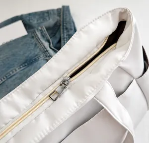 Close-up of smooth silver metal zipper and neat stitching on off-white nylon tote bag