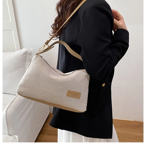 Dettaglio della borsa a tracolla in tela beige con finiture in pelle marrone e metallo oro