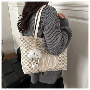 Detail view of large beige tote bag with M-letter jacquard and plush cloud charm on shoulder