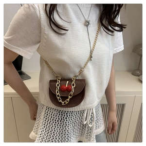 Detail of a brown leather saddle bag featuring unique 3D red cherry accents and gold chains