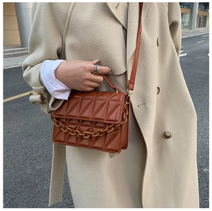 Detail of brown quilted leather crossbody bag with chunky chain decor and top handle