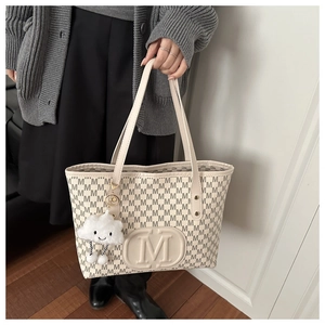 Close-up of beige tote bag with M-pattern print and a white fluffy cloud charm