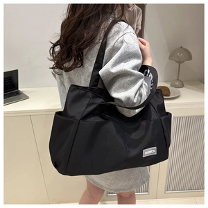 Detail of black nylon tote bag showing side pocket and fashion label in home office setting