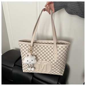 Detail of warm beige tote bag with M-pattern texture and white plush cloud charm