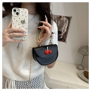 Close-up of a black semi-round crossbody bag with red cherry accents and gold chains