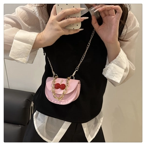Close-up of pink crossbody bag with cherry accents and gold chain strap detail