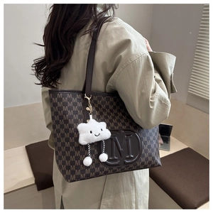 Detail of dark brown tote bag featuring embossed M logo and white cloud plush charm
