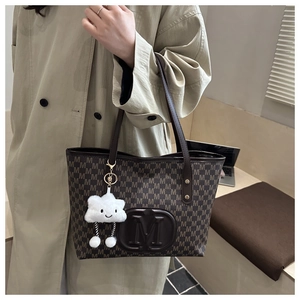 Detail of large brown tote bag with M-letter print and plush cloud charm accessory