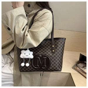 Detail of large brown tote bag with M monogram pattern and plush cloud charm accessory