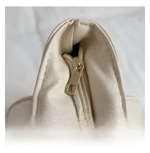Close-up of smooth gold zipper and pebble leather texture on cream tote bag