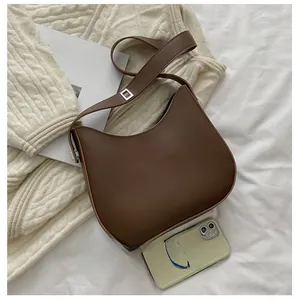 Sac seau demi-lune en cuir marron avec bandoulière réglable à côté d'un pull douillet