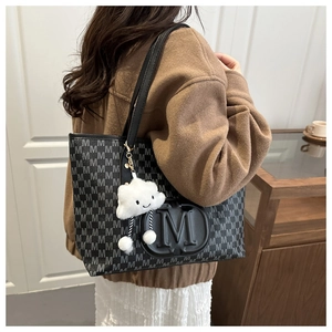 Detail of printed tote bag with leather M logo and white plush cloud charm on shoulder