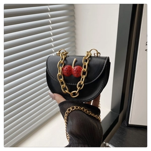 Detailed macro shot of a black saddle bag with luxury cherry accents and gold chain strap