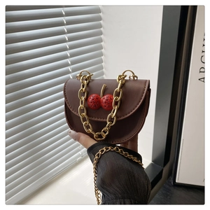 Close-up of brown saddle bag featuring 3D cherry decor and thick gold chain strap