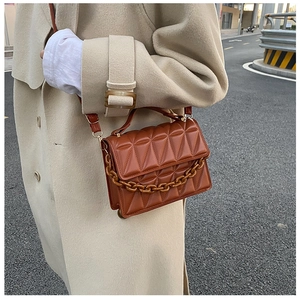 Detail of caramel quilted crossbody bag with amber chain handle on wool coat