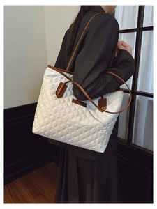 Detail of white quilted tote bag with brown leather straps and fashion label
