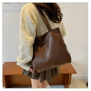 Detail of a large dark brown tote bag showing supple leather texture and wide shoulder strap